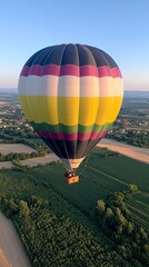 Obraz premium Colorful hot air balloon soaring over green fields and distant village at sunset