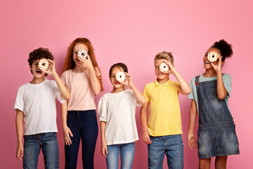 Obraz premium Diverse schoolkids holding yummy donuts in front of their faces on pink background