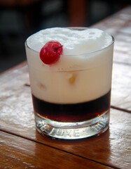 Elegant close-up of a creamy Amaretto cocktail in an old-fashioned glass, topped with a frothy milk-based layer and garnished with a maraschino cherry.