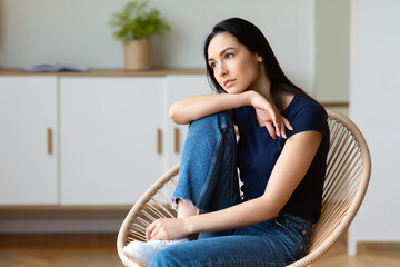Thoughtful Girl Sitting In Cozy Modern Armchair Relaxing On Weekend At Home. Empty Space For Text