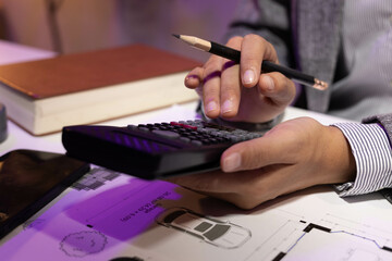 A woman is sitting at a desk with two model houses in front of her. She is holding a pencil and she...