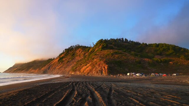 Stunning sunset surf waves USAL Beach campground tents 4wd trucks cars PNW Lost Coast Trail aerial drone California rugged dramatic untouched coastline mist fog clouds nature landscape pan left