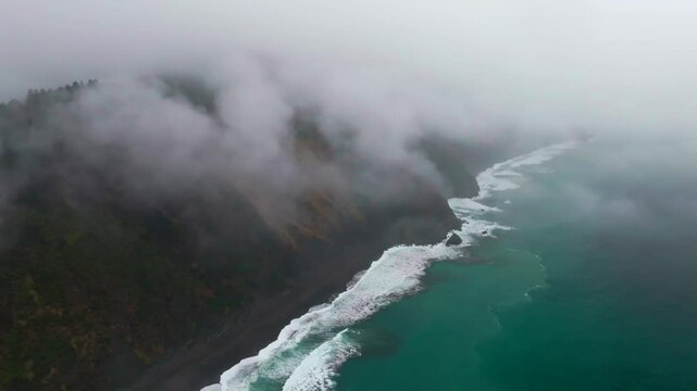 Waves crashing boulder rocks rugged coastline black sand USAL Beach Campground Lost Coast Trail California aerial drone fog mist rain cloudy layer morning Pacific Ocean mountainside backwards motion