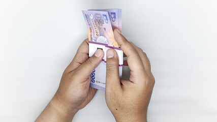 two hands counting Indonesian banknotes in the 10,000 rupiah denomination