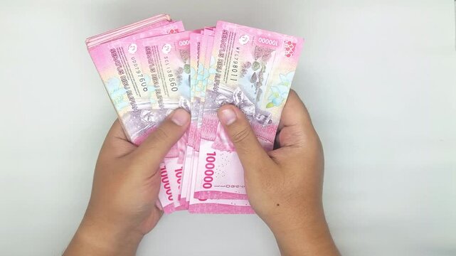 two hands counting Indonesian banknotes in the 100,000 rupiah denomination