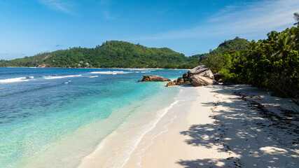 Rocky formations along a pristine beach surrounded by lush green hills. Baie Lazare. Seychelles, Mahe.