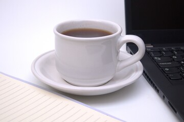 Cup of coffee, notebook and laptop on white table