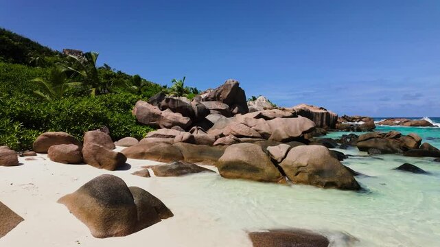 Granite boulders rise from a white sandy beach surrounded by lush tropical greenery and turquoise waters. Anse Cocos. Seychelles, La Digue.