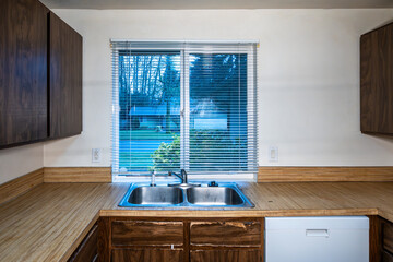 1970s vintage kitchen, dark brown cabinets, wood grain laminate counter tops, white walls and stainless steel sink, rental home interior damage after the tenant moves out, housing market
