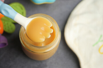 Creamy baby food in a jar with a playful spoon on a table
