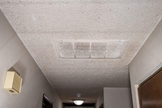 Large white air intake vent in hallway ceiling covered in dust and cobwebs along with asbestos containing popcorn ceiling, rental home interior dirty mess after the tenant moves out, housing market
