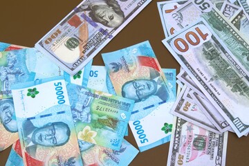 stacks of 100 dollar bills and 50,000 rupiah on a brown table
