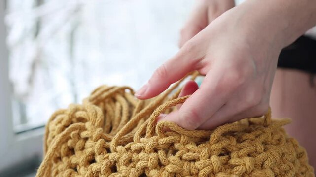Creative home project, macrame crafting. Female hands intertwine thick yellow cotton strings into an intricate design. Handmade rope art and wall decor. Artistic fiber work and bohemian handicraft