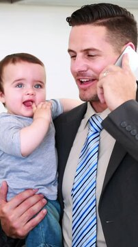 Father holding his baby son before work and talking on phone