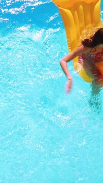 Overhead of brunette sitting on lilo in pool on sunny day