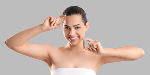 Beautiful young woman holding ampules on grey background