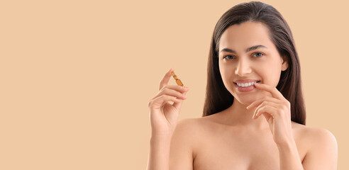 Beautiful young woman holding ampule on beige background