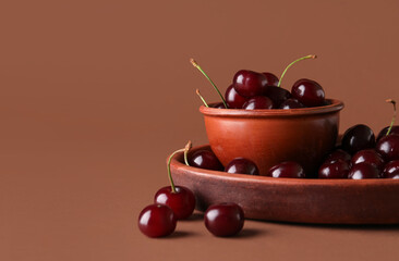 Bowl and plate with sweet cherries on brown background