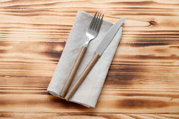 Modern silver cutlery with napkin on brown wooden background