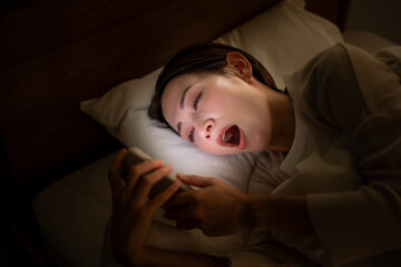 ベッドに入ってスマホを使う女性