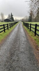 Fototapeta premium Serene gravel driveway lined with black fences leading to a rustic barn