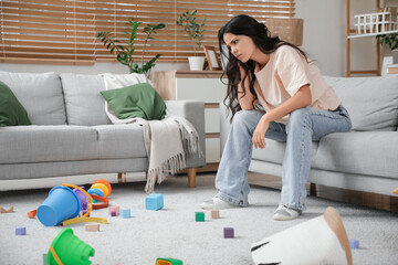 Tired young mother resting among scattered children's toys at home. Stress concept