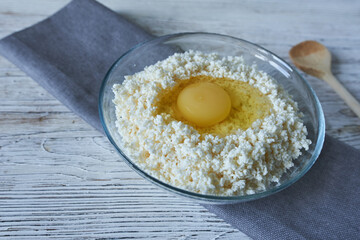 Cottage cheese with egg in glass bowl on white wooden background.