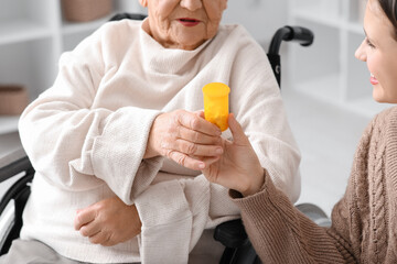 Senior woman in wheelchair taking pills from nurse at home, closeup
