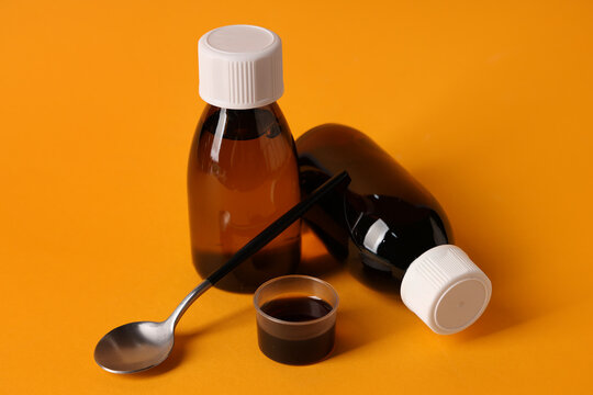 Bottles and measuring cup of cough syrup with spoon on orange background