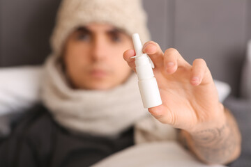 Ill young man with nasal drops lying in bedroom, closeup