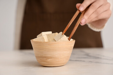 Woman with bowl of tasty tofu cheese on table, closeup