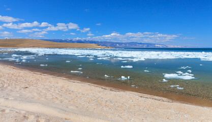 Baikal Lake in sunny May day. Sandy beach of Olkhon Island.  White ice floats floating on blue water of the shallow Elga Bay of Small Sea Strait. Beautiful spring landscape. Natural season background