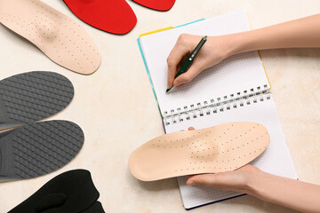 Woman with orthopedic insoles writing in notebook on light background