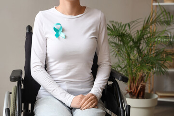 Young woman in wheelchair with turquoise ribbon at home. Cervical Health Awareness Month