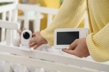 Woman putting baby monitor on crib in children's bedroom, closeup
