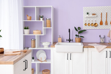 Interior of stylish kitchen with utensils on pegboard, sink and shelving unit
