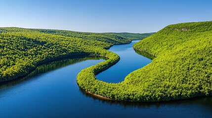 Fototapeta premium Winding river curves through verdant hills beneath a clear sky