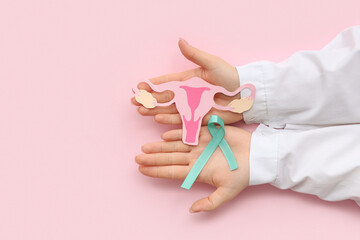 Female doctor hands with turquoise ribbon and paper uterus on pink background. Cervical Health...