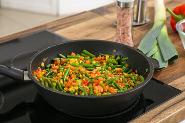 Frying pan with roasted vegetables on stove in kitchen