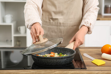 Young woman frying tasty vegetables in kitchen