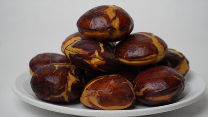 A collection of raw jengkol placed on a white plate with a white base and background (isolated white).