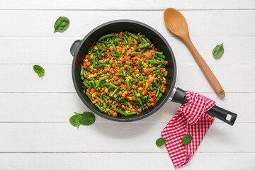 Frying pan with tasty roasted vegetables on white wooden background