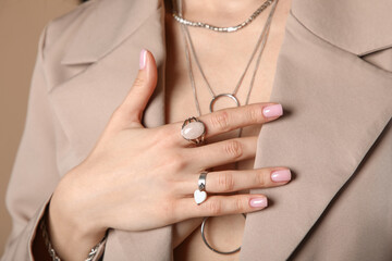 Pretty young woman in stylish blazer with silver rings and necklace on beige background, closeup