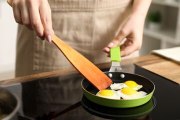 Woman frying quail eggs on electric stove in kitchen, closeup