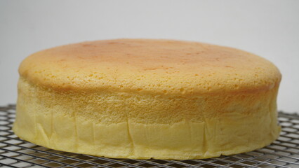 A whole Japanese Cheese Cake placed on a cooling rack with a white base and background (isolated white).