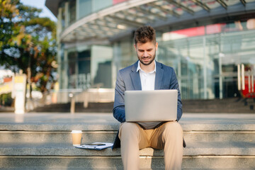Handsome unshaven businessman walking with laptop, tablet and smartphone on city street.