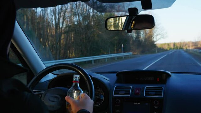Close up of hand holding and unscrewing a drink while driving on a highway, reckless behavior in shade of trees