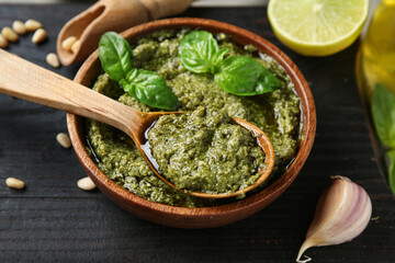 Bowl of delicious pesto sauce with spoon, basil leaves and garlic, closeup