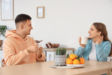 Handsome young man and his girlfriend drinking tea at table in kitchen together