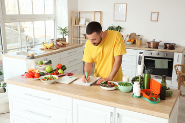 Handsome young man with fresh vegetables and notebook planning his diet in kitchen. Healthy food...